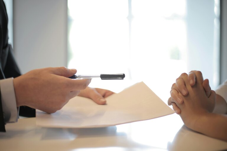 Personne tendant un stylo-bille et un contrat à une autre personne